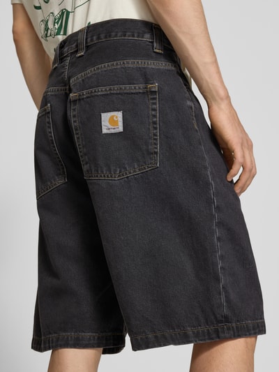 Männermodel trägt Jeansshorts mit Eingrifftaschen Modell 'Brandon' von Carhartt Work In Progress in Schwarz, Reine Baumwolle, Relaxed-Fit, Ganzkörperansicht Rückansicht. Bundweite bei Größe M: 44 cm, Innenbeinlänge bei Größe M: 25 cm.