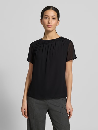 Modelka kobieca nosi Regular Fit Blusenshirt mit semitransparenten Ärmeln von s.Oliver BLACK LABEL, czarny, krój regular fit, okrągły dekolt, krótki transparentny rękaw, lekka tekstura szyfonowa, widok całej sylwetki z przodu.