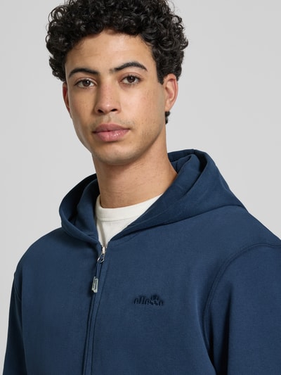 Męski model nosi Sweatjacke mit Kapuze Modell 'TAURASI' od Ellesse, bawełniany miks, luźny krój, z kapturem, zamek, haft z logo, kieszenie, ściągacze, długość pleców 66 cm, długość rękawa 64 cm, zbliżenie na górną część ciała.