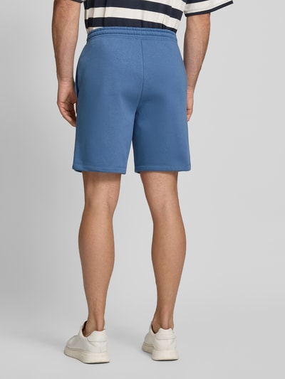 Männermodel trägt Sweatshorts mit Logo und elastischem Bund von GAP aus Baumwoll-Mix in Blau, Regular-Fit, Eingrifftaschen, Ganzkörperansicht Rückansicht.