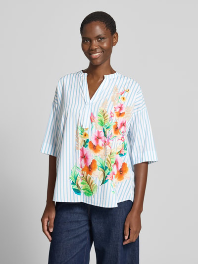 Kobiece model prezentuje Relaxed Fit Bluse mit Motiv-Print von Emily Van den Bergh, bawełna, dekolt w serek, rękaw o dł. 1/2, długość tyłu w rozmiarze 36: 48 cm, długość rękawów w rozmiarze 36: 24 cm, kolorowe paski i nadruk z motywem, widok z przodu na całą sylwetkę.