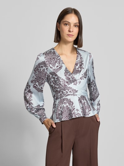 Vrouwenmodel draagt blouse met peplum-zoom Model 'Rista' van Neo Noir in lichtblauw met donkerbruin patroon, getailleerde pasvorm, v-hals, met lange mouwen, ruglengte bij maat 36: 55 cm, mouwlengte bij maat 36: 65 cm, detailopname bovenlichaam.