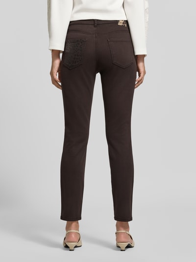 Frauenmodel trägt Slim Fit Jeans mit Lyocell-Anteil von Marc Cain in Dunkelbraun, 5-Pocket-Design, elastischer Material-Mix, 7/8-Länge, Ganzkörperansicht Rückansicht.
