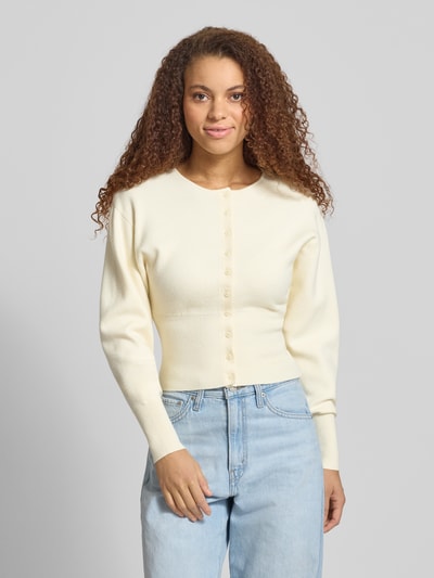 Modelka kobieca nosi Slim Fit Cardigan aus Viskose-Mix od Gina Tricot, krój regular fit, dzianinowa faktura, kremowy kolor, guziki, szerokie i elastyczne ściągacze, długość tyłu w rozmiarze S: 48 cm, długość rękawa: 59 cm, widok całej sylwetki z przodu.