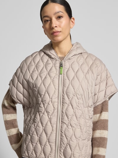 Frauenmodel trägt Steppjacke im kurzärmeligen Design von Fuchs Schmitt in Beige mit Kapuze, Reißverschluss und Eingrifftaschen, Nahaufnahme Oberkörper.