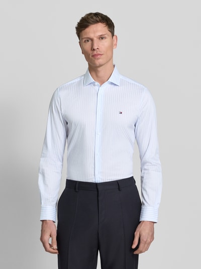 Männermodel trägt Slim Fit Businesshemd aus Baumwoll-Mix von Tommy Hilfiger Tailored mit feinen Streifen, Kentkragen, Logo-Stitching, Ganzkörperansicht von vorne.