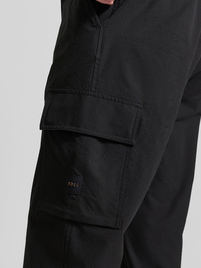 Männermodel trägt Relaxed Fit Cargohose mit Gürtelschlaufen Modell 'SRACKY' von BOSS Orange in Optik: Unifarben, Label-Patch, Cargotaschen, Nahaufnahme Oberschenkel.
