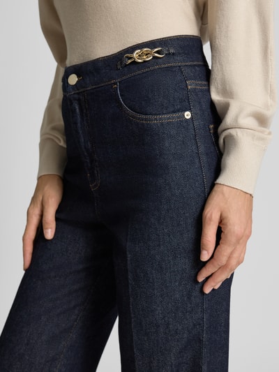 Frauenmodel trägt Straight Fit Jeans mit Knopfverschluss von Emporio Armani, dunkles Blau, Metallic-Details, 5-Pocket-Design, Bügelfalten, Nahaufnahme Oberkörper.