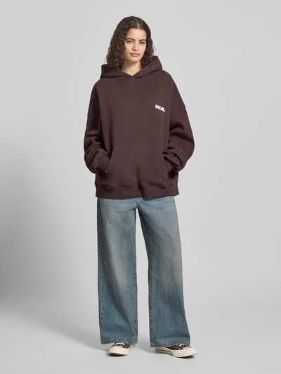 Frauenmodel trägt Oversized Hoodie mit Label-Prints und Känguru-Tasche von Karo Kauer, reine Baumwolle, lockere Jeans, Ganzkörperansicht von vorne.