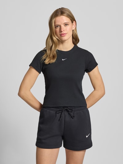 Frauenmodel trägt Cropped T-Shirt in Ripp-Optik mit Logo von Nike aus Baumwoll-Elasthan-Mix, schwarzer Farbton, Rundhalsausschnitt, Rückenlänge bei Größe S 48 cm, Ganzkörperansicht von vorne.