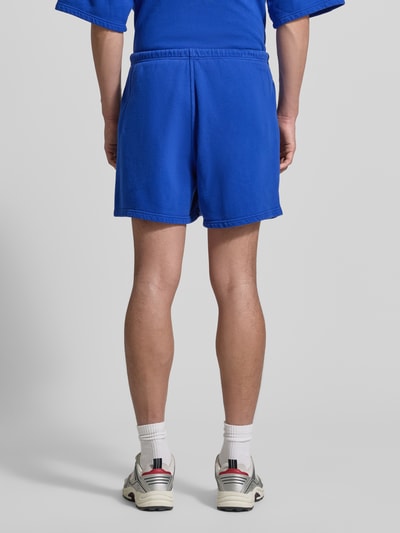 Männermodel trägt Shorts mit Logo Modell 'PLIZZY' von American Vintage in Blau aus Reine Baumwolle, Relaxed-Fit, Ganzkörperansicht Rückansicht.