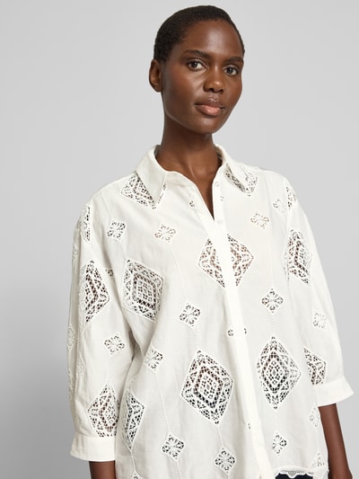Frauenmodel trägt Regular-Fit Damen Bluse mit Häkelspitze Modell 'MURIEL' von Bash, weiß, verdeckte Knopfleiste, Nahaufnahme Oberkörper. Rückenlänge 65 cm, Ärmellänge 40 cm, Hemdblusenkragen, 3/4-Arm, feine Textur mit grafischen Mustern.
