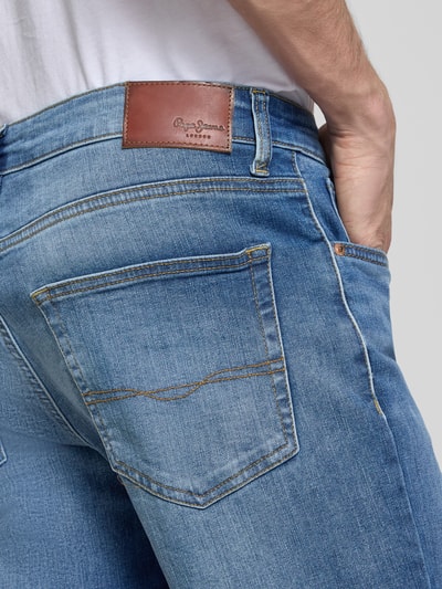 Mannenmodel draagt Regular Fit Jeansshorts uit katoenmix model 'CASH' van Pepe Jeans met denimlook, 5-pocket-design, metalen labelapplicatie, contraststiksels en riemlussen, detailopname rugzijde.