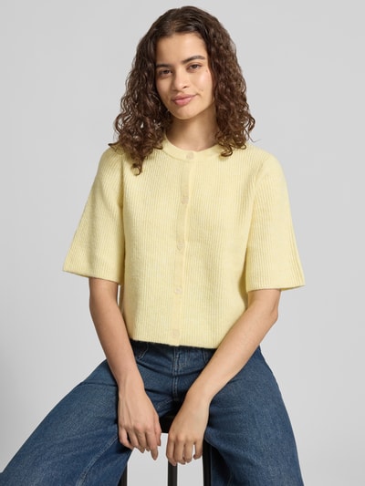 Frauenmodel trägt Boxy Fit Strickjacke aus Rippstrick Modell 'SILLY' von PIECES in meliertem Gelb, kurzarm, Materialmix mit Woll-Anteil, Nahaufnahme Oberkörper.