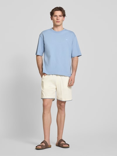 Männermodel trägt Shorts mit umstochener Kante von REVIEW in Creme mit elastischem Bund und Eingrifftaschen, Ganzkörperansicht von vorne. Baumwoll-Mix mit Viskose-Anteil, Regular Fit, Bundweite 42 cm, Innenbeinlänge 19 cm.