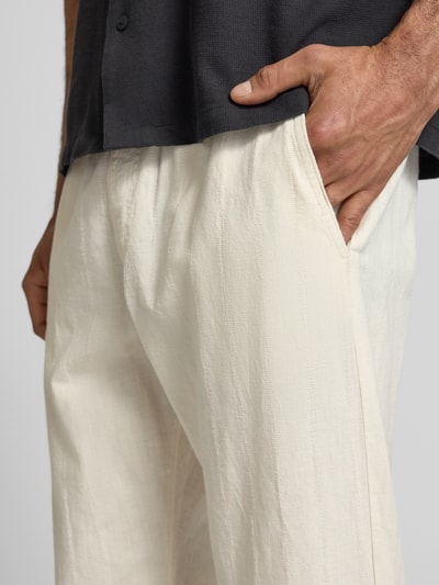 Männermodel trägt Relaxed Fit Hose aus Baumwoll-Leinen-Mix Modell 'KANE' von Jack & Jones in Creme mit Tunnelzug, Gesäßtasche, Nahaufnahme Oberkörper. Bundweite 41 cm, Innenbeinlänge 77 cm.