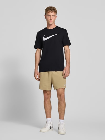 Männermodel trägt Regular Fit T-Shirt aus reiner Baumwolle von Nike in Schwarz mit großem weißen Logo, glatte Textur, Ganzkörperansicht von vorne. Herren T-Shirt von Nike