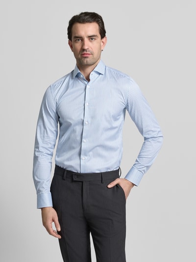 Männermodel trägt Slim Fit Businesshemd aus reiner Baumwolle Modell 'HANK' von BOSS mit feinen blauen Streifen, Ganzkörperansicht von vorne.