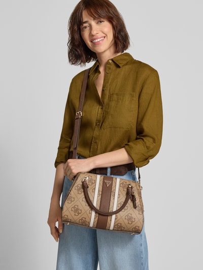 Frauenmodel trägt Handtasche in Leder-Optik Modell 'Noelle' von GUESS, beige-braune Farben, Logo-Detail, Nahaufnahme Oberkörper. Geteiltes Hauptfach mit Magnetverschluss, abnehmbarer Schulterriemen, Maße 26x22x12 cm, Länge Schulterriemen 122 cm.