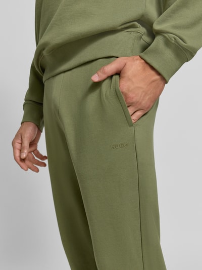 Männermodel trägt olivgrüne Regular Fit Jogginghose aus reiner Baumwolle Modell 'Dayote232' von HUGO, Nahaufnahme Oberschenkel. Herren Jogginghose von HUGO.