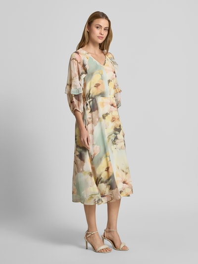 Frauenmodel trägt Midikleid mit V-Ausschnitt von Soyaconcept, Leicht taillierte Passform, Midilänge, 3/4-Arm, Rüschenbesatz, Rückenlänge 128 cm, Brustweite 40 cm, Ärmellänge 42 cm, pastellfarbene, fließende Textur, florales Muster, Ganzkörperansicht von vorne.