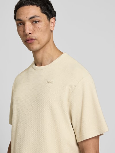 Männermodel trägt Relaxed Fit T-Shirt mit Strukturmuster von Forét, Reine Baumwolle, Logo-Stitching, Rundhalsausschnitt, Nahaufnahme Oberkörper. Rückenlänge bei Größe M: 69 cm