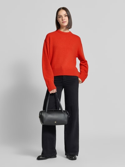 Vrouwenmodel draagt Relaxed Fit Strickpullover aus Schurwolle-Kaschmir-Mix van Lanius, Dames, mix van scheerwol en kasjmier, relaxed fit, los model, ribboorden, ruglengte maat 36: 56 cm, mouwlengte maat 36: 57 cm, feloranje, zwarte broek, zwarte tas, Ganzkörperansicht van voren.