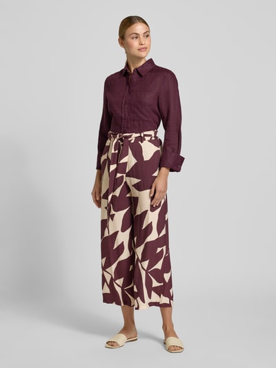 Frauenmodel trägt Stoffhose aus Viskose-Mix mit Bindegürtel Modell 'PLUMAS' von Mango, relaxed Fit, Allover-Blattmuster, Ganzkörperansicht von vorne.