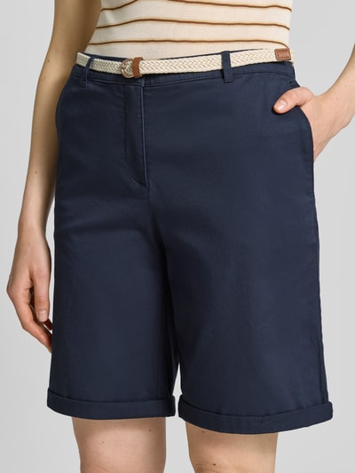 Frauenmodel trägt dunkelblaue Chino-Bermudas mit Gürtel von Christian Berg Woman aus reiner Baumwolle, Nahaufnahme Oberschenkel.