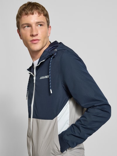 Männermodel trägt Jacke mit Kapuze und Reißverschluss Modell 'RUSH' von JACK & JONES, regular fit, Logo, Tunnelkoord, steekzakken, Nahaufnahme Oberkörper. Ruglengte maat M 68 cm, schouderbreedte 46 cm, borstwijdte 55 cm, mouwlengte 68 cm.