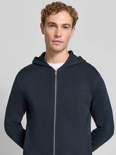 Męski model nosi Regular Fit Pullover aus reiner Baumwolle od Marc O'Polo o ciemnogranatowym kolorze, lekko widoczna faktura tkaniny, zamek z przodu, bluza z kapturem, zbliżenie na górną część ciała, kontekst: sweter męski Marc O'Polo.