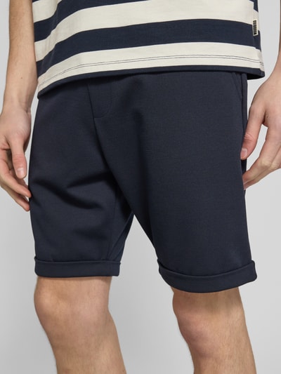 Männermodel trägt Sweatshorts mit elastischem Bund und Gesäßtasche von MCNEAL, dunkle Farbe, strukturierte Textur, Nahaufnahme Oberkörper. Material-Mix mit Viskose-Anteil, Regular Fit, Tunnelzug, Bundweite 44 cm, Innenbeinlänge 21 cm.