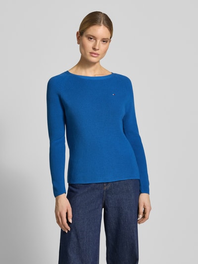 Vrouwenmodel draagt Regular Fit gebreide pullover uit puur katoen van Tommy Hilfiger in effen blauw met logo-opschrift, tricotlook, lange mouw, ronde hals, rompzoom en mouwboord geribd, materiaalverwerking knitwear, Ganzkörperansicht van voren.