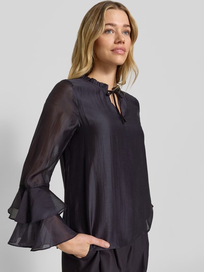 Frauenmodel trägt Regular Fit Bluse aus Lyocell-Mix mit Volants von Comma in dunklem Farbton, Schlüsselloch-Ausschnitt, Rückenlänge 58 cm, Ärmellänge 60 cm, Ganzkörperansicht von vorne.