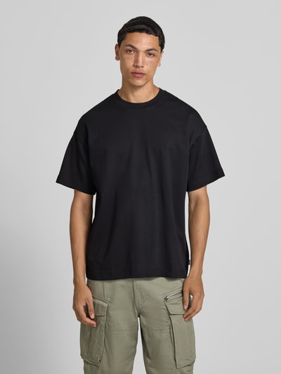 Männermodel trägt Jack & Jones Herren T-Shirt mit Baumwoll-Mix und Stretch-Anteil, Relaxed-Fit, Modell 'BARRON', schwarzer Stoff, Ganzkörperansicht von vorne.