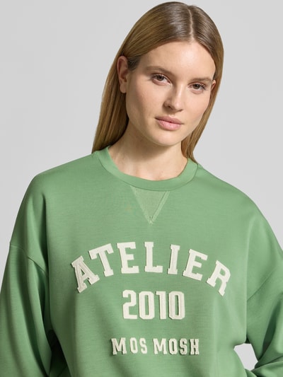 Kobiece model nosi Relaxed Fit Sweatshirt aus Viskose-Mix Modell 'Nima' von MOS MOSH, elastyczna mieszanka wiskozy, detal z logo, okrągły dekolt, elastyczne wykończenia, zbliżenie górnej części ciała.