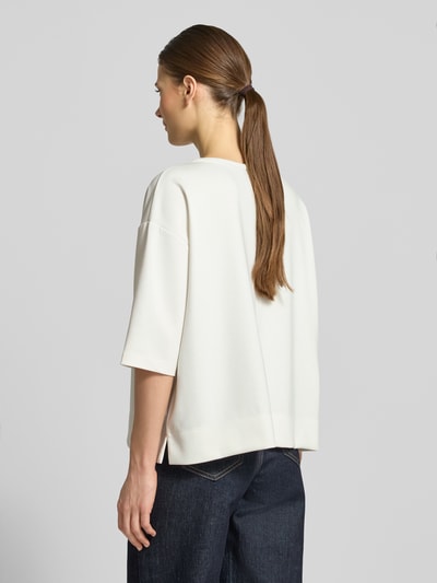 Frauenmodel trägt T-Shirt mit Rundhalsausschnitt und Logo von monari in Offwhite, lockerer Relaxed Fit, Material-Mix, Rückansicht Ganzkörperansicht.