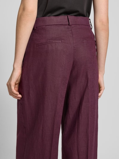 Frauenmodel trägt Straight Fit Leinenhose mit Bügelfalten Modell 'Tempoli' von Mango in dunklem Violett, Reine Leinen, Ganzkörperansicht Rückansicht.
