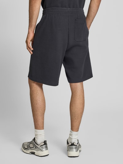 Männermodel trägt Relaxed Fit Shorts mit Strukturmuster von KARL KANI aus Baumwoll-Mix, dunkler Farbton, Elastischer Bund, Ganzkörperansicht Rückansicht.