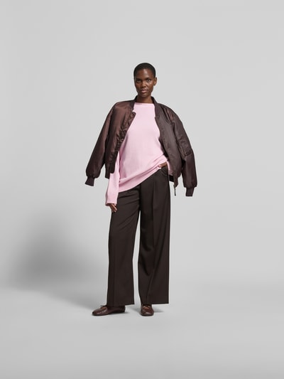 Frauenmodel trägt Oversized Wollpullover aus Woll-Mix von Nanushka in Rosa, Strick-Optik, Stehkragen, gerippte Abschlüsse, Ganzkörperansicht von vorne.