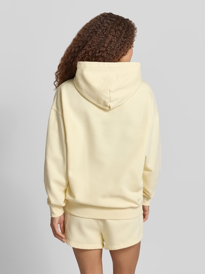Frauenmodel trägt Oversized Hoodie mit Label-Stitching Modell 'CLARITA' von Pegador aus Baumwoll-Mix in Hellgelb, Känguru-Tasche, Ganzkörperansicht Rückansicht.