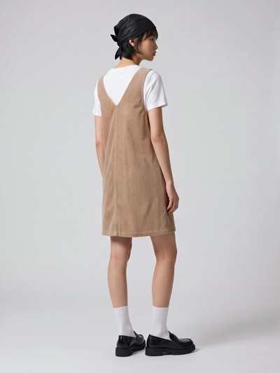 Frauenmodel trägt Minikleid aus Cord mit aufgesetzten Taschen von MOP DENIM in Beige, unifarben, gerade geschnittener Saum, Ganzkörperansicht Rückansicht.