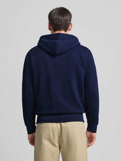 Męski model nosi Bluza rozpinana z wyhaftowanym logo i kieszenią kangurka od Polo Ralph Lauren, mieszanka bawełny, krój regular fit, kaptur z tunelem, zamek błyskawiczny, długość tyłu 70 cm, długość rękawa 65 cm, widok całej sylwetki od tyłu.