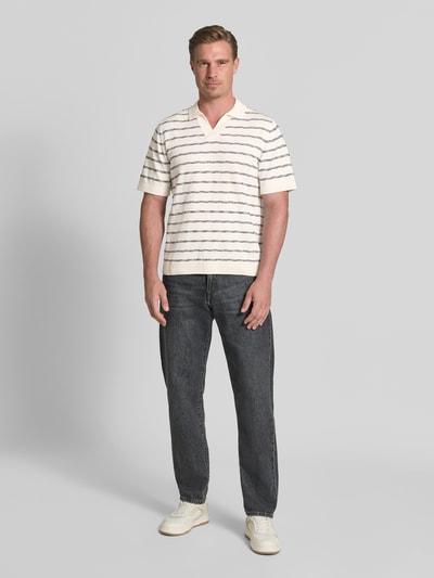 Männermodel trägt Regular Fit Poloshirt aus reiner Baumwolle von Tom Tailor, cremeweiß mit blauen Streifen, dunkle Jeans, Ganzkörperansicht von vorne. Herren Poloshirt von Tom Tailor.