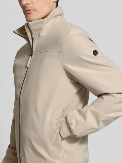 Männermodel trägt Regular Fit Jacke mit Stehkragen Modell 'Alvin' von Didriksons in Beige, dezente Struktur, Nahaufnahme Oberkörper.