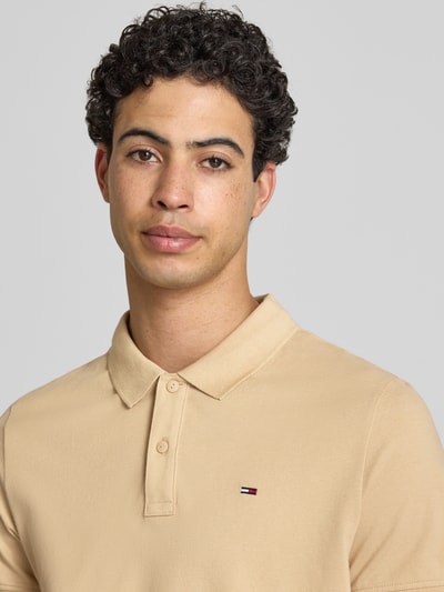 Männermodel trägt Regular Fit Poloshirt Modell 'TJM SLIM PLACKET POLO EXT' von Tommy Jeans in Beige mit Logo Stitching, Nahaufnahme Oberkörper.
