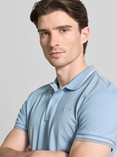 Męski model nosi Slim Fit Poloshirt mit Kontraststreifen od Geox, bawełniany mix, krój slim fit, jasnoniebieski, polo kołnierzyk, krótka listwa guzikowa, kontrastowe paski, długość tyłu w rozmiarze M 69 cm, zbliżenie na górną część ciała.