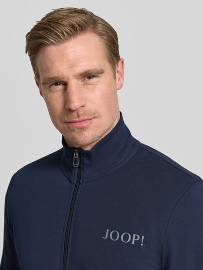 Männermodel trägt Sweatjacke mit Logo und Stehkragen von JOOP! Collection, dunkelblauer Baumwoll-Elasthan-Mix, Regular-Fit, Nahaufnahme Oberkörper.