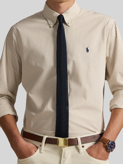 Męski model nosi Slim Fit Freizeithemd aus Baumwoll-Mix od Polo Ralph Lauren, efekt: wzór w paski, wyhaftowane logo, krój slim fit, kołnierzyk typu button down, listwa guzikowa na całej długości, długi rękaw z mankietem sportowym, mieszanka bawełny i cieniowanej przędzy, kolor beżowy i biały, tekstura gładka, Ganzkörperansicht z przodu.