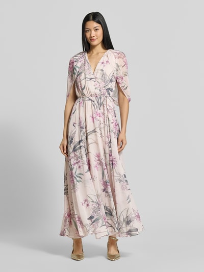 Vrouwenmodel draagt avondjurk met V-hals Model 'Jodie' van Forever New, chiffon, getailleerde pasvorm, wikkellook, halflange vleermuismouwen, maxilengte, tailleband, onderrok, ruglengte maat 36: 135 cm, borstwijdte maat 36: 30 cm, lichtroze met bloemendessin, Ganzkörperansicht von vorne.